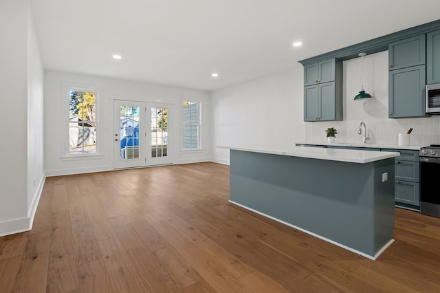 kitchen featuring a kitchen island, sink, backsplash, stainless steel appliances, and light wood-type flooring