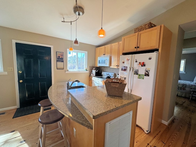 kitchen with stone counters, decorative light fixtures, a center island with sink, light wood-style floors, and white appliances