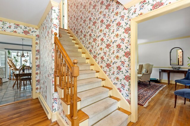 stairs with hardwood / wood-style floors, ornamental molding, and an inviting chandelier