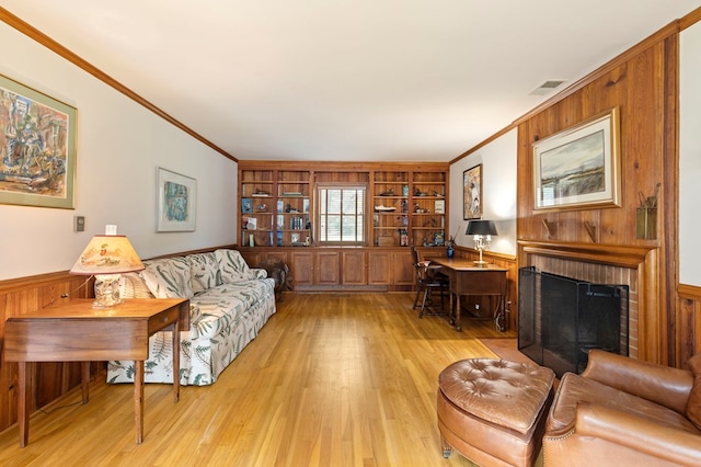 living room with built in shelves, crown molding, light wood-type flooring, and a brick fireplace