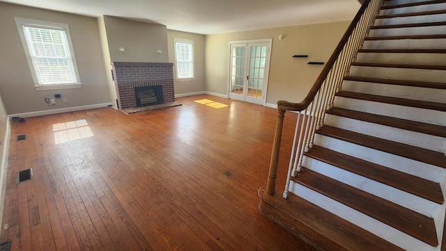 unfurnished living room with hardwood / wood-style floors, a healthy amount of sunlight, a fireplace, and french doors