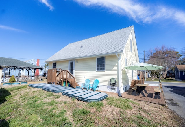 rear view of property featuring a lawn, roof with shingles, and a deck