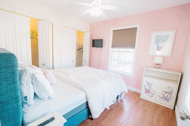 bedroom featuring baseboards, light wood-style flooring, two closets, and a ceiling fan