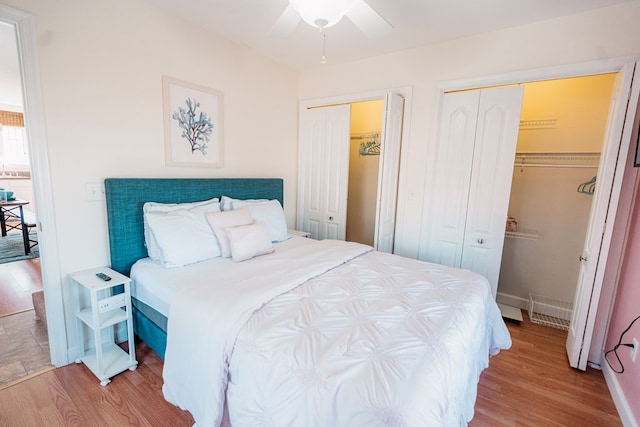 bedroom with wood finished floors, visible vents, two closets, and baseboards