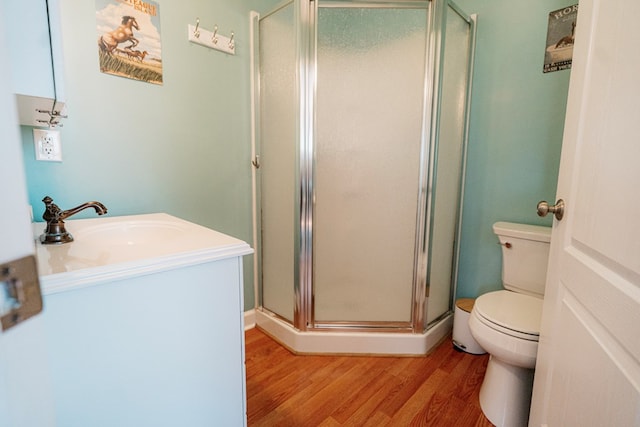 bathroom featuring vanity, toilet, wood finished floors, and a stall shower