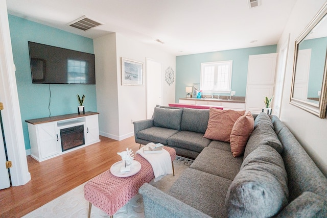 living room featuring a fireplace, visible vents, light wood-type flooring, and baseboards