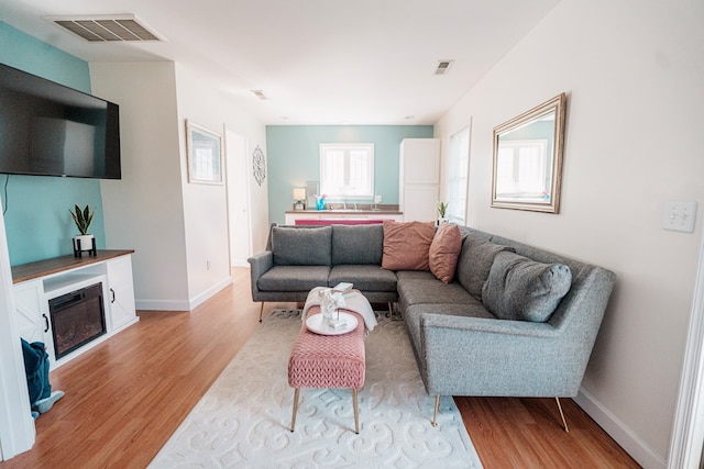 living room featuring a glass covered fireplace, light wood-style floors, visible vents, and baseboards