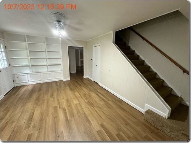 unfurnished living room with built in shelves, ceiling fan, and light hardwood / wood-style flooring