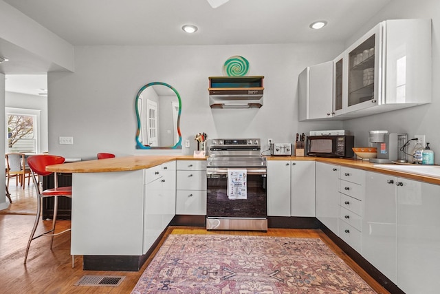 4282 Main St, Chincoteague, VA 23336 - kitchen with stainless steel electric stove, a peninsula, black microwave, white cabinetry, and wood finished floors
