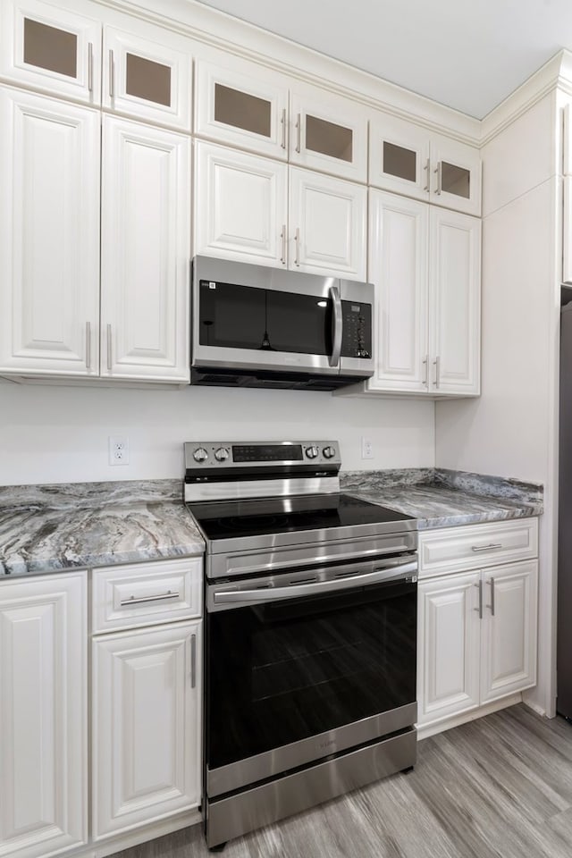 kitchen featuring stone countertops, stainless steel appliances, white cabinetry, and light hardwood / wood-style flooring