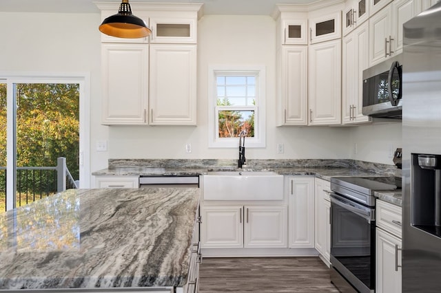 kitchen with dark stone counters, stainless steel appliances, sink, pendant lighting, and white cabinets