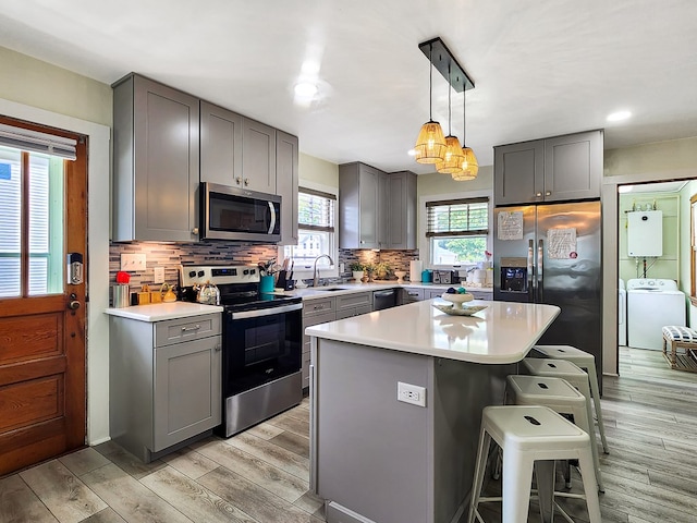 kitchen with gray cabinetry, stainless steel appliances, washer / dryer, a kitchen island, and a breakfast bar area