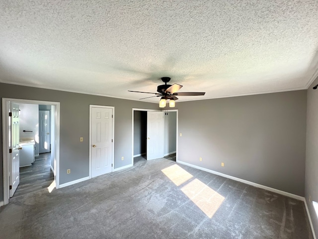 unfurnished bedroom featuring two closets, dark colored carpet, ceiling fan, ornamental molding, and a textured ceiling