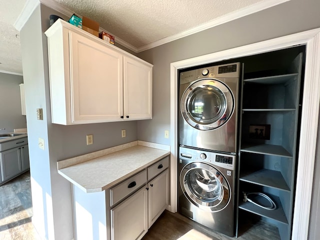 clothes washing area with sink, cabinets, stacked washing maching and dryer, a textured ceiling, and ornamental molding