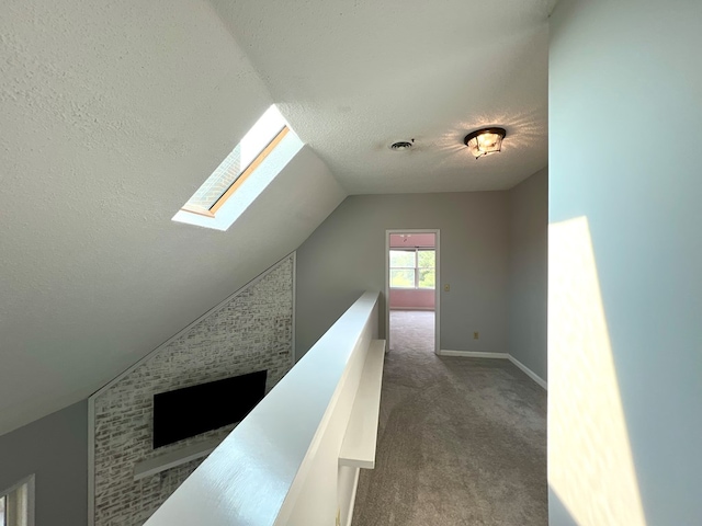 corridor with lofted ceiling with skylight, carpet, and a textured ceiling