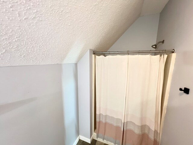 bathroom with a textured ceiling, vaulted ceiling, and curtained shower