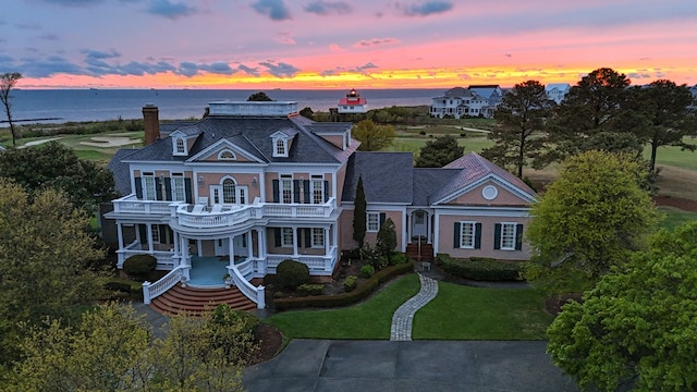 view of front of home with covered porch, a water view, a balcony, and a lawn