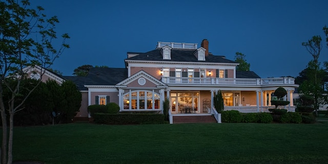 back of house at twilight with a yard, a balcony, covered porch, and a chimney