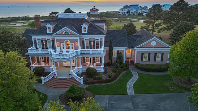 view of front of house featuring french doors, a balcony, a water view, covered porch, and a lawn