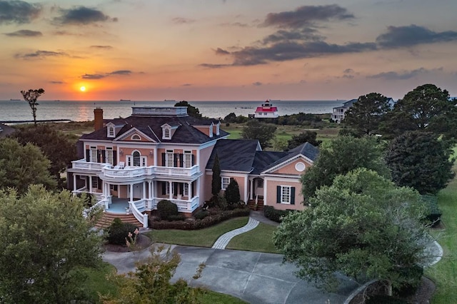 view of front facade featuring a water view, a porch, concrete driveway, a chimney, and a balcony