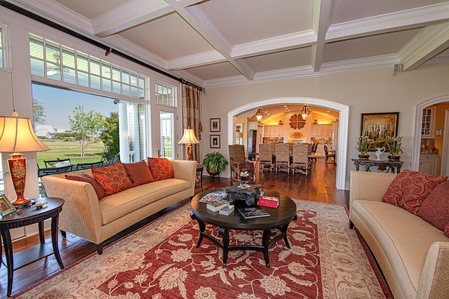 living area with beamed ceiling, ornamental molding, wood finished floors, arched walkways, and coffered ceiling