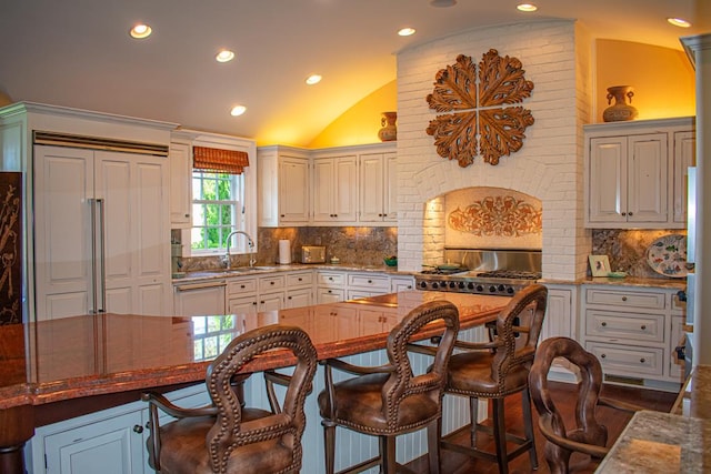 kitchen featuring decorative backsplash, vaulted ceiling, sink, paneled built in refrigerator, and white cabinetry