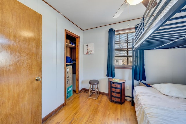 bedroom with baseboard heating, wood finished floors, a ceiling fan, and baseboards