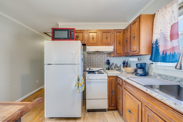 kitchen with white appliances, brown cabinetry, light wood-type flooring, under cabinet range hood, and a sink