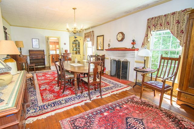 dining area featuring a fireplace, a notable chandelier, ornamental molding, and wood finished floors