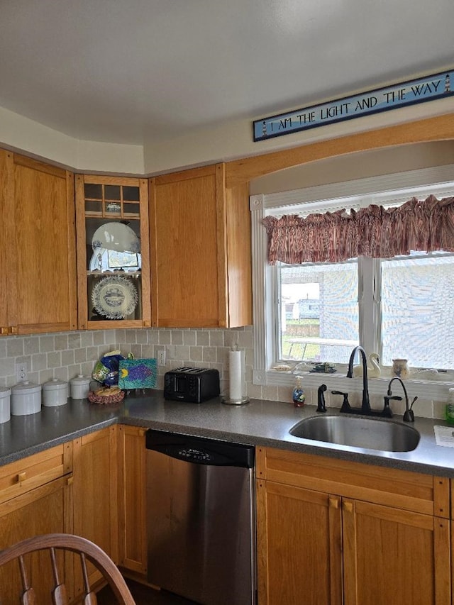 kitchen featuring backsplash, dark countertops, dishwasher, a sink, and glass insert cabinets