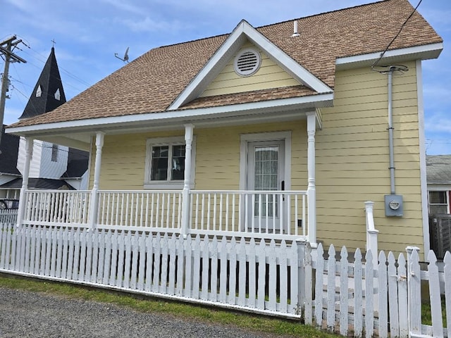 view of front facade featuring a porch, fence, and a shingled roof