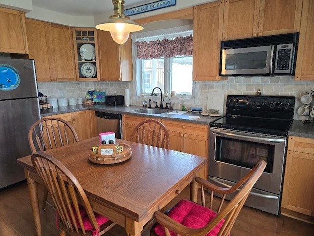 kitchen with dark countertops, a sink, dark wood finished floors, stainless steel appliances, and backsplash