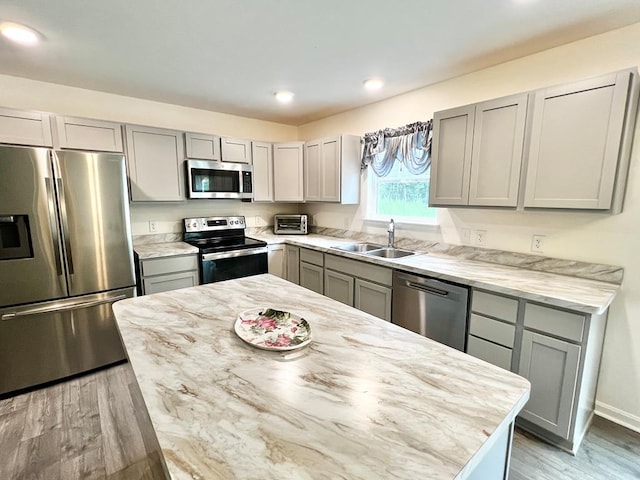 kitchen featuring sink, gray cabinets, light stone countertops, appliances with stainless steel finishes, and light hardwood / wood-style floors