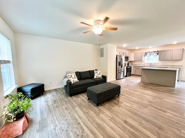 living room with light hardwood / wood-style flooring, ceiling fan, and a healthy amount of sunlight