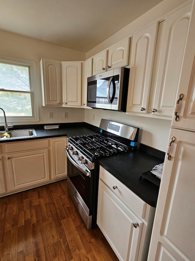 kitchen with a sink, dark countertops, appliances with stainless steel finishes, and dark wood-style floors