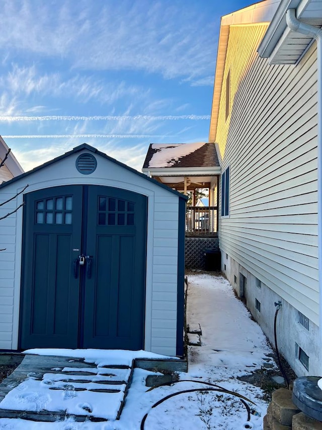 snow covered structure featuring a storage shed and an outbuilding