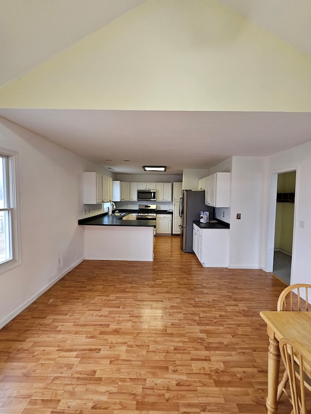 kitchen featuring dark countertops, white cabinetry, a peninsula, and stainless steel appliances