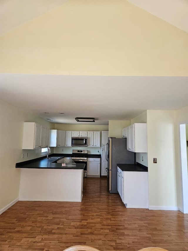 kitchen featuring a sink, dark countertops, dark wood finished floors, appliances with stainless steel finishes, and a peninsula