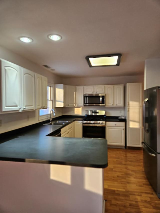 kitchen with sink, appliances with stainless steel finishes, dark hardwood / wood-style floors, white cabinets, and kitchen peninsula