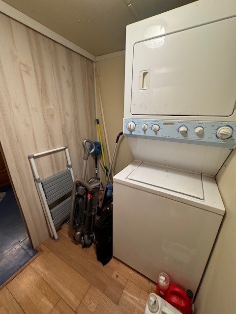 clothes washing area with stacked washer / drying machine, light wood-type flooring, and wooden walls