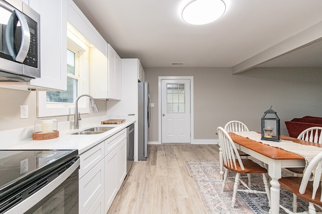 kitchen with white cabinets, light wood-type flooring, stainless steel appliances, and sink