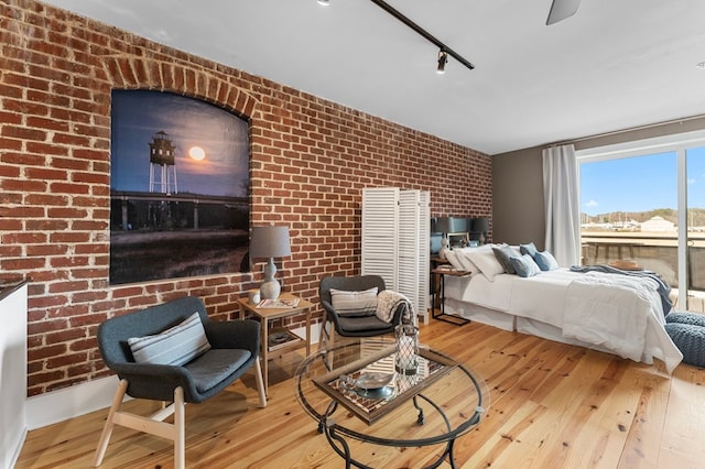 bedroom featuring track lighting, brick wall, and wood finished floors