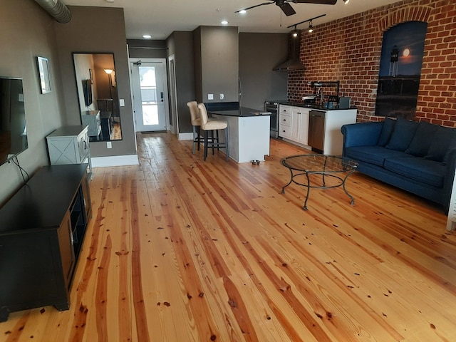 living room with brick wall, rail lighting, sink, ceiling fan, and light wood-type flooring