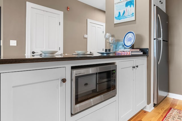 kitchen featuring dark countertops, light wood-style floors, appliances with stainless steel finishes, and white cabinets