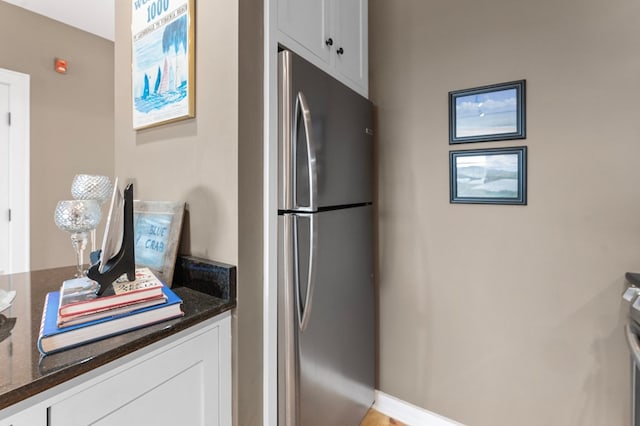 kitchen with dark stone counters, freestanding refrigerator, and white cabinets