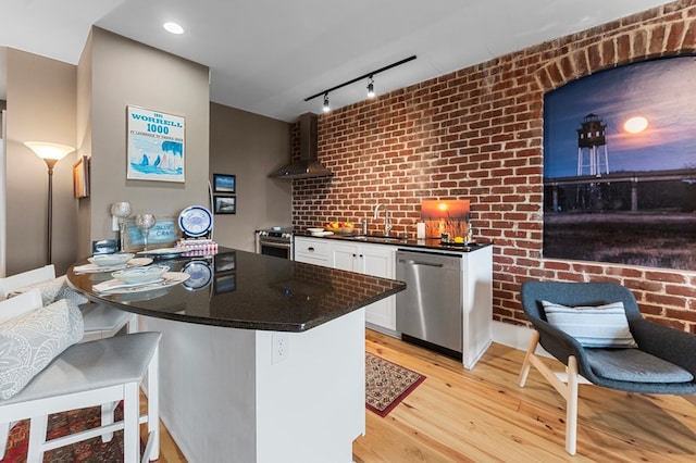 kitchen with white cabinetry, sink, stainless steel appliances, wall chimney range hood, and light hardwood / wood-style flooring