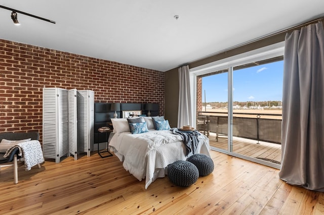 bedroom featuring brick wall, access to exterior, and light hardwood / wood-style flooring