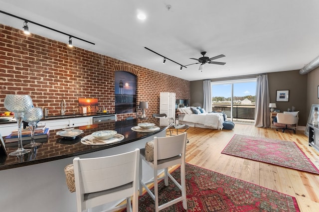 interior space featuring ceiling fan, brick wall, light wood-style flooring, and track lighting