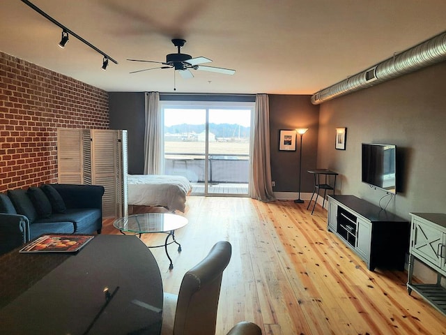 living room featuring light hardwood / wood-style floors, rail lighting, ceiling fan, and brick wall