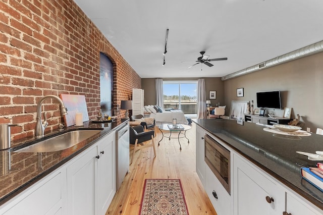 kitchen featuring white cabinets, appliances with stainless steel finishes, open floor plan, dark stone countertops, and a sink